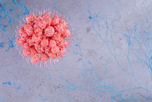 Glass holder with a portion of popcorn candy next to decorative blue branches on marble background. High quality photo